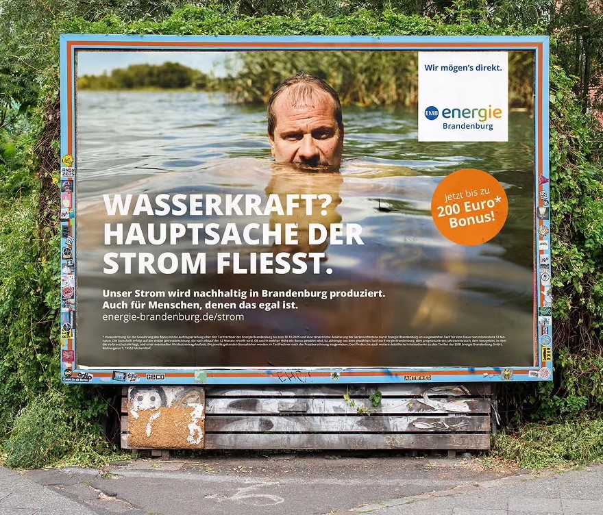 Werbung für die Energie Brandenburg mit dem Slogan 'Wasserkraft? Hauptsache der Strom fließt.', zeigt einen Mann, der im Wasser steht, umgeben von grüner Landschaft.
